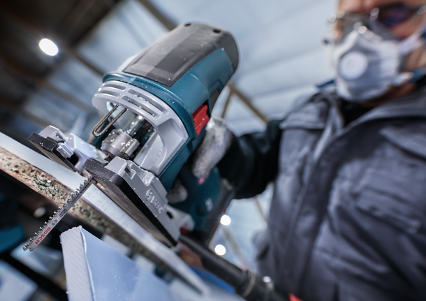 配戴安全設備的人員使用曲線鋸切割一塊材料。