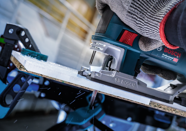 一名佩戴安全設備的人使用曲線鋸切割一塊木板。