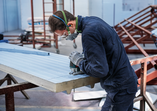 配戴安全設備的人員使用曲線鋸在絕緣板上切割凹槽。