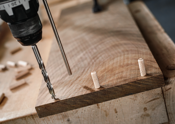 用鑽頭在木板上鑽孔，並在附近插入銷釘。