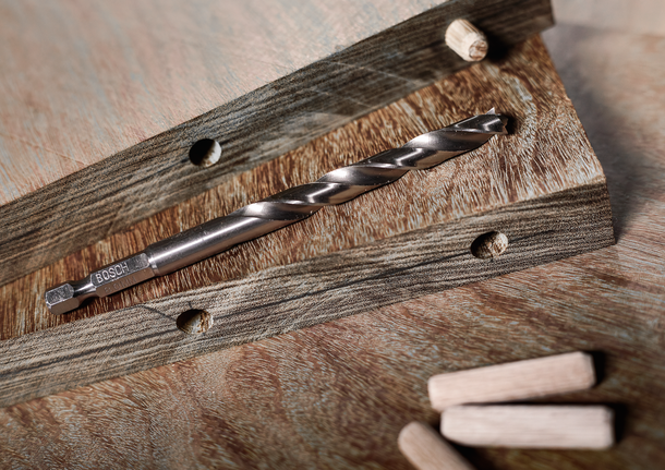 鑽頭放在木板上，附近有鑽孔和鬆脫的銷釘。