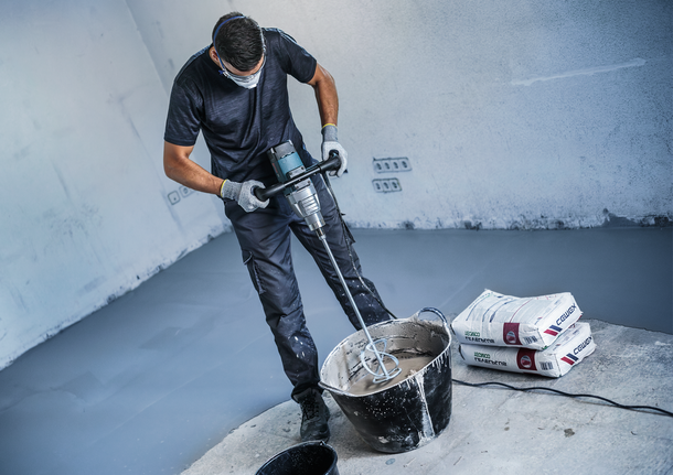 一名配戴安全設備的人員使用電動工具攪拌桶中的砂漿。