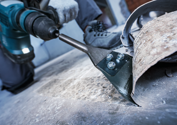 一名配戴安全設備的人員正在使用電動鑿子去除地板材料。