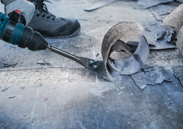 配戴安全設備的人員使用電動工具去除舊地板材料。