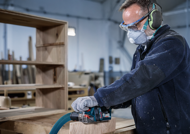 一名佩戴安全設備的工人在車間打磨木板。