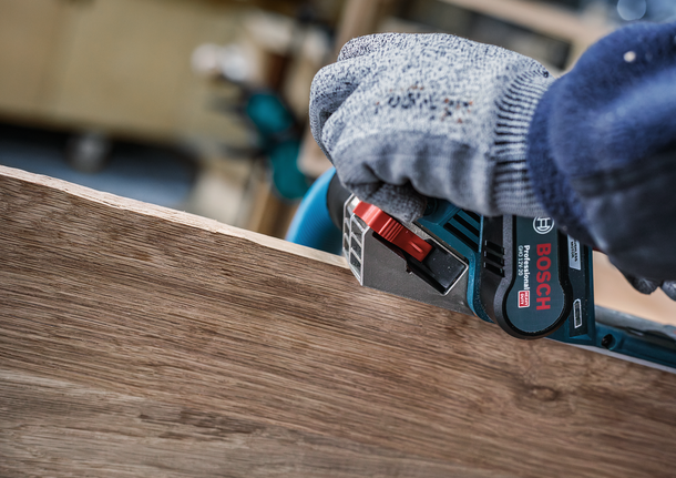 配戴安全設備的人員使用電動工具打磨木板的邊緣。
