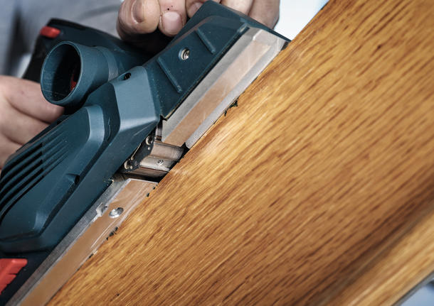 一個人使用電刨來打磨木板的邊緣。