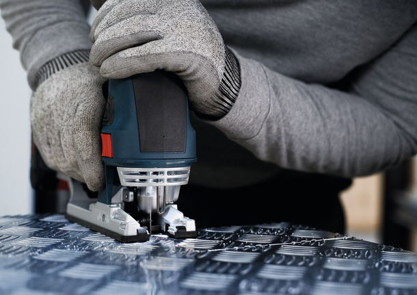 配戴安全設備的人員使用曲線鋸切割有圖案的金屬。