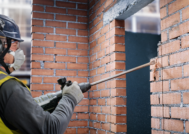 配戴安全裝備的人員用破碎錘鑿開磚牆。