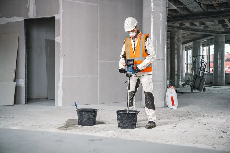 配戴安全設備的人員使用攪拌裝置混合桶中的材料。.