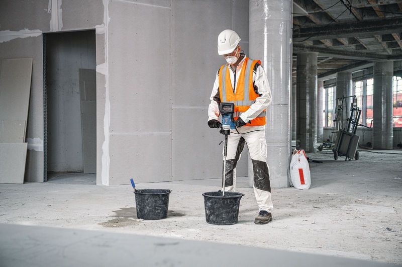 配戴安全設備的人員使用攪拌裝置混合桶中的材料。.