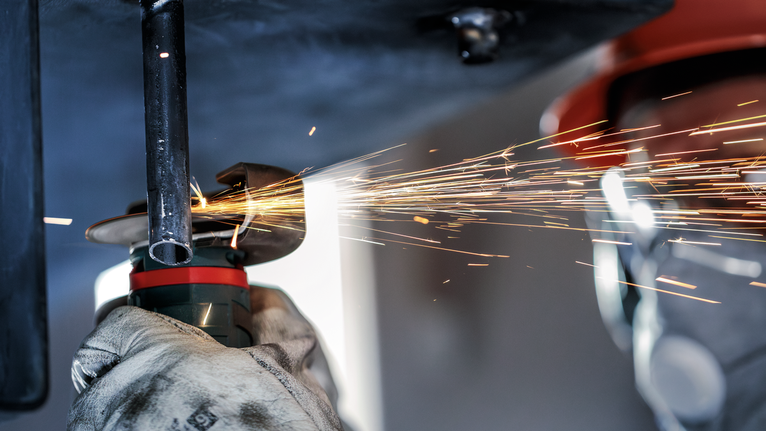 配戴安全設備的人員在火花飛濺的情況下研磨金屬管。.