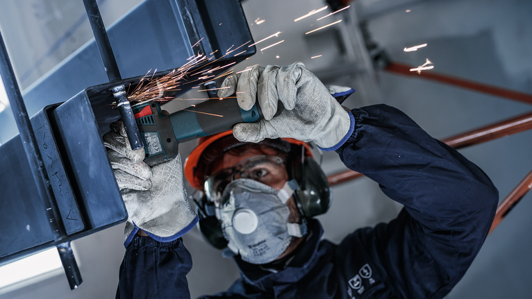 一名配戴安全設備的人正在研磨金屬，產生火花。