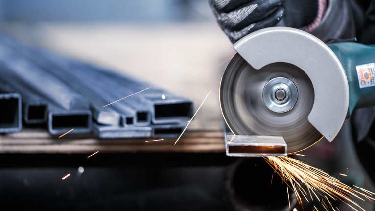 佩戴安全設備的人用圓鋸切割金屬管，火花四濺。