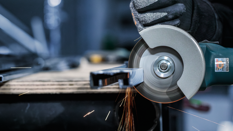 配戴安全設備的人使用角磨機切割金屬，產生火花。