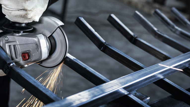 配戴安全設備的人使用角磨機切割金屬，產生火花。.