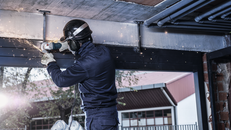 配戴安全設備的人在室內研磨金屬梁，產生火花。.