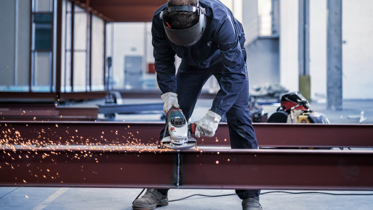 配戴安全設備的人磨削鋼樑，產生明亮的火花。.