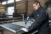 一名配戴安全設備的工人在車間的工作台上鑽金屬網。
