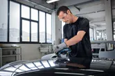 配戴安全設備的人員正在使用隨機軌道打磨機打磨汽車車頂。
