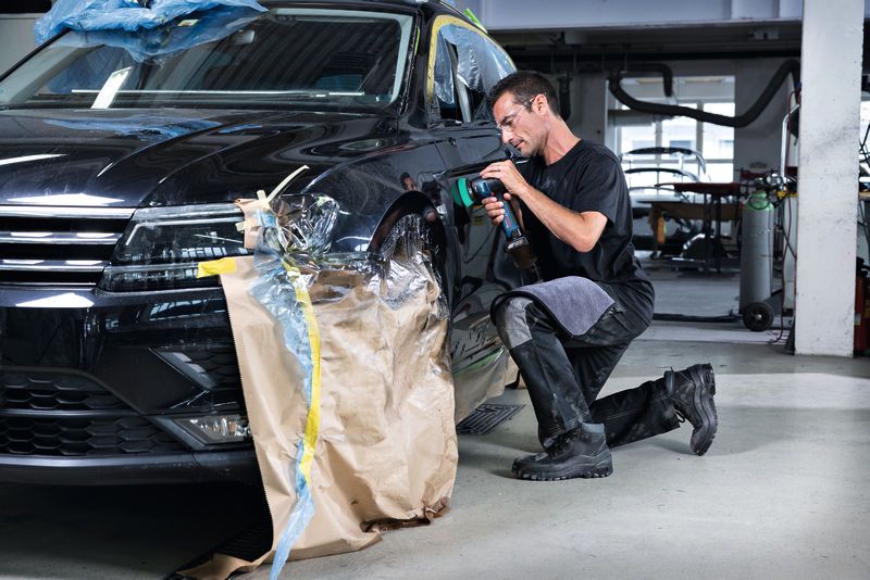 汽車修理店裡，一名配戴安全設備的人員正在使用拋光機拋光汽車擋泥板。.