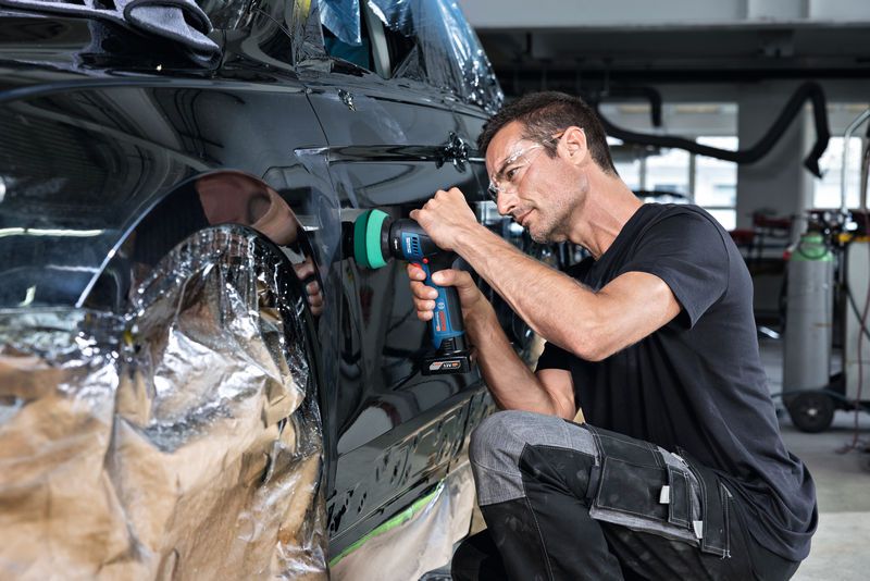 一名配戴安全設備的人員正在使用無線工具擦拭車門。.