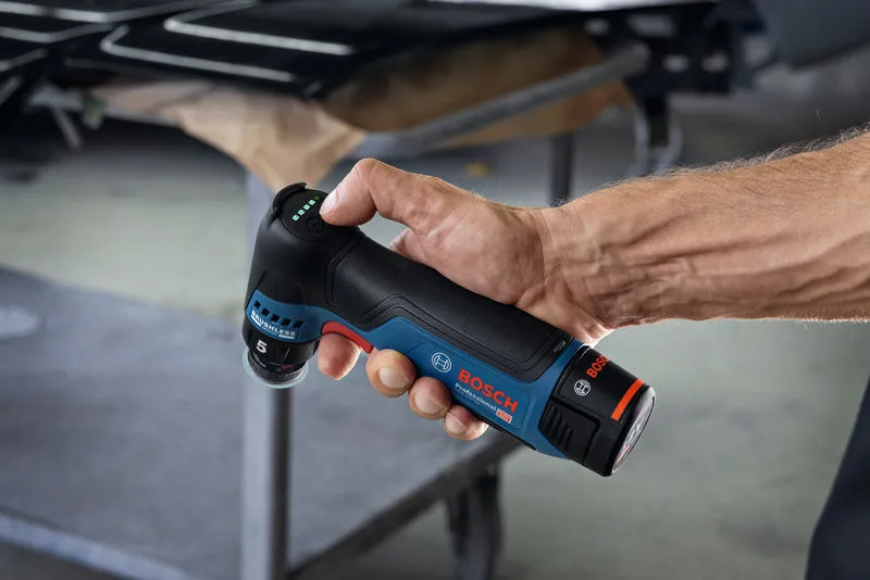 一個人在車間裡拿著一台無線隨機軌道砂光機。.