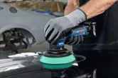 一名佩戴安全設備的人正在使用無線拋光機拋光汽車錶面。