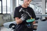一名配戴安全設備的人員在汽車修理廠內對無線拋光機進行拋光。