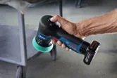 一個人在金屬推車附近拿著一台帶有綠色泡沫墊的無線拋光機。