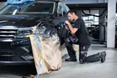 汽車修理廠裡，一名配戴安全設備的人員正在擦拭汽車擋泥板。