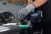 一名佩戴安全設備的人正在使用無線拋光機拋光汽車錶面。