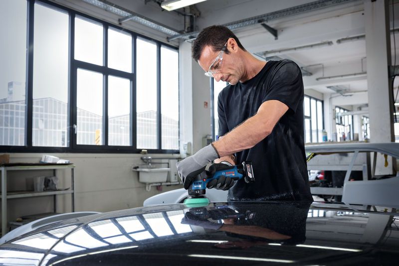 一名配戴安全設備的人員在汽車修理廠內擦拭汽車引擎蓋。.