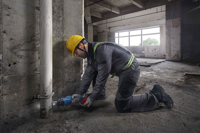 一名配戴安全設備的人員使用往復鋸切割混凝土牆附近的管道。.