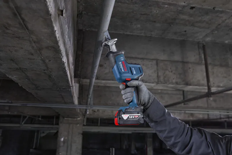 一名配戴安全設備的人員正在用往復鋸切割頭頂上的金屬管道。.