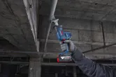 一名配戴安全設備的人員正在用往復鋸切割頭頂上的金屬管道。.