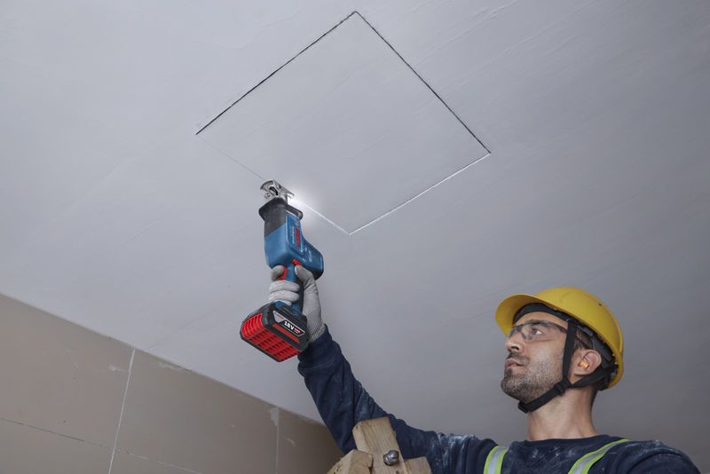 一名配戴安全設備的人員正在用往復鋸切割天花板。.