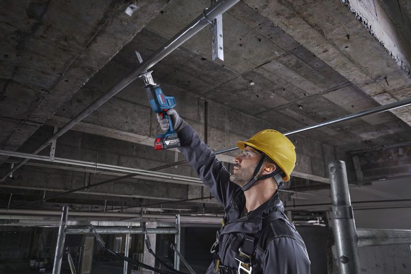 一名佩戴安全設備的人員使用往復鋸切割頭頂上的金屬管道。.