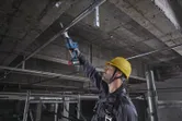 一名佩戴安全設備的人員使用往復鋸切割頭頂上的金屬管道。