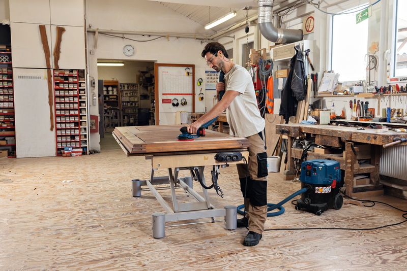 一名配戴安全設備的人員正在使用無線隨機軌道砂光機打磨木質表面。.