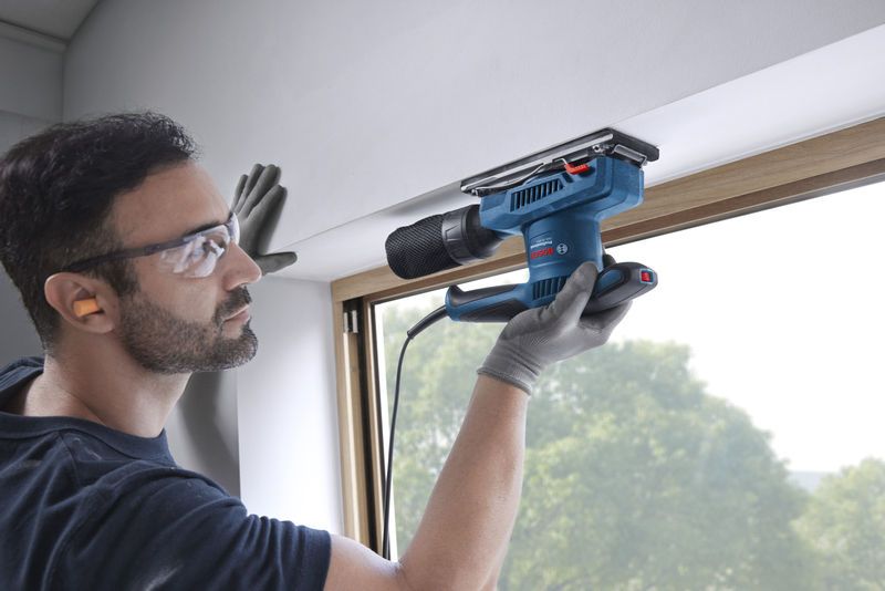 一名配戴安全設備的人員正在使用軌道砂光機打磨窗框。.