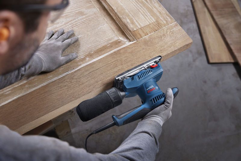 一名配戴安全設備的人員正在用軌道砂光機打磨木門。.