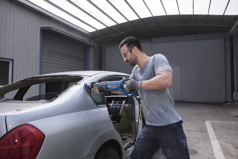 配戴安全設備的人員使用往復鋸切割汽車的後窗框架。.