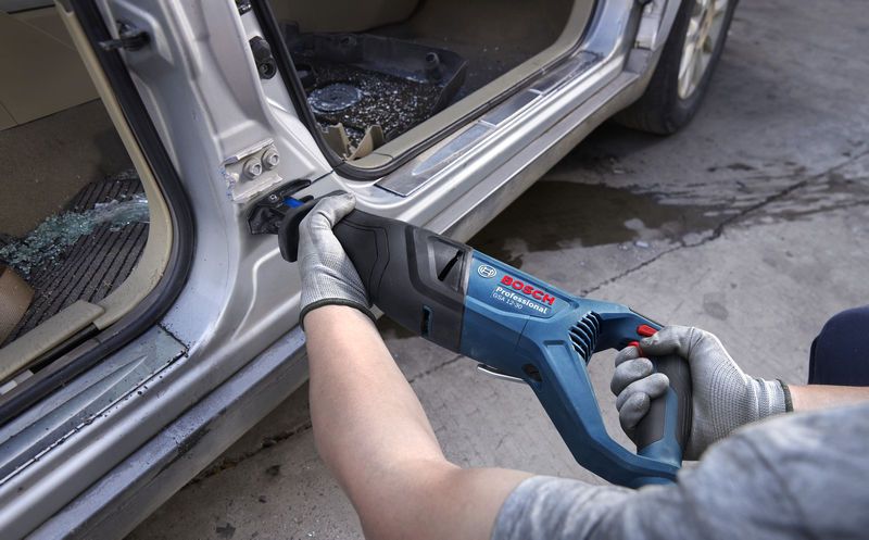 一名配戴安全設備的人員使用往復鋸切割車門框上的金屬。.