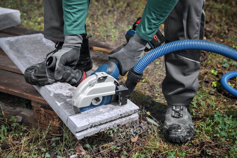 一名佩戴安全設備的人員使用帶有除塵裝置的大型角磨機切割混凝土。.