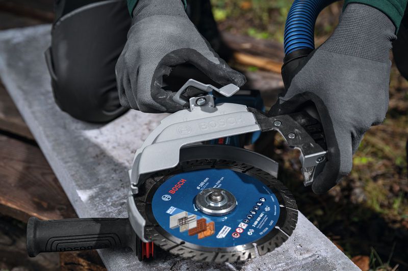 一名配戴安全設備的人員將除塵防護罩安裝到大型角磨機上。.