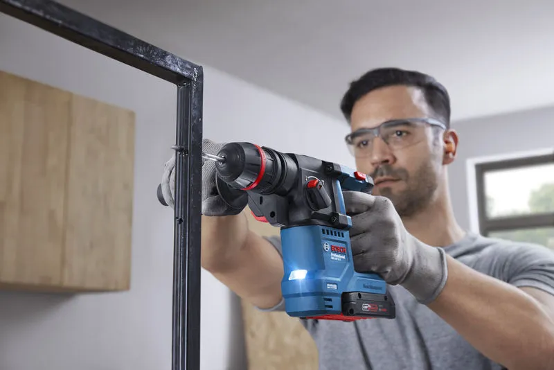 一名佩戴安全設備的人員使用無線旋轉錘在金屬框架上鑽孔。.