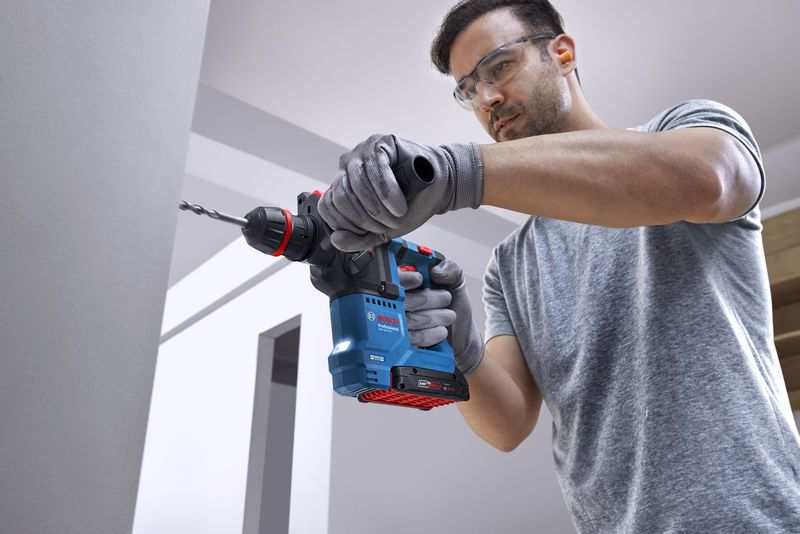 GBH 18V-18 X 一名佩戴安全設備的人員使用無線旋轉錘在混凝土牆上鑽孔。.