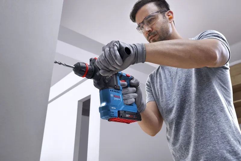 一名佩戴安全設備的人員使用無線旋轉錘在混凝土牆上鑽孔。.