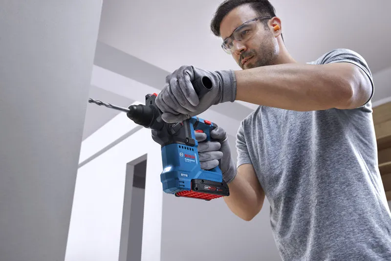 配戴安全設備的人員使用旋轉錘在牆上鑽孔。.